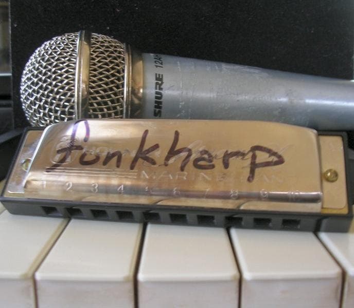 A harmonica with the word funkharp written across the metal cover, sitting on piano keys in front of a Shure microphone.