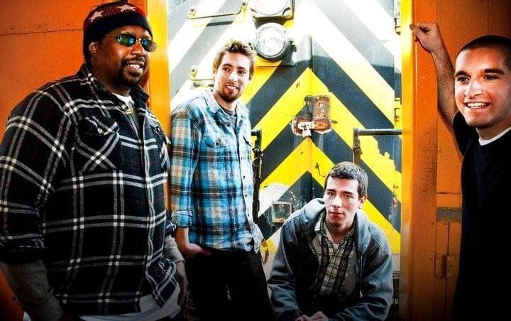 Four Funkharp members standing in the doorway of a yellow and black rail car.