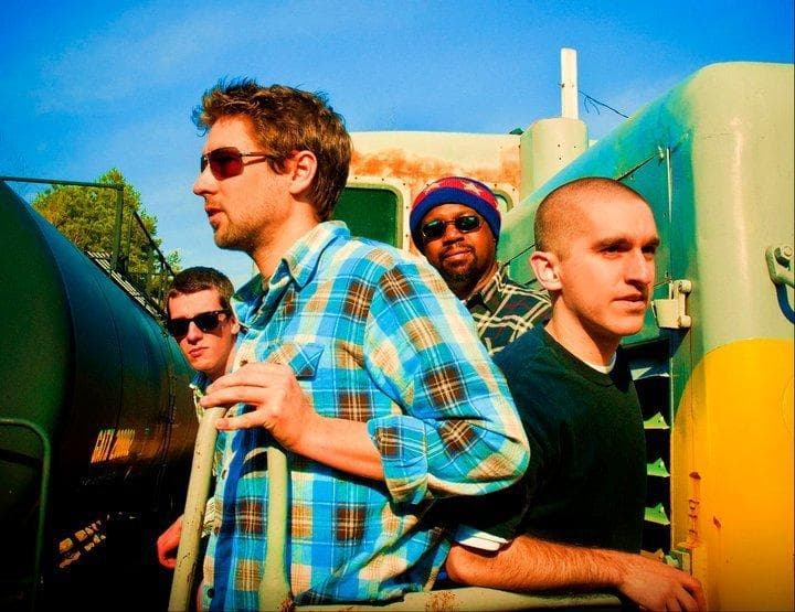 Four Funkharp members on a yellow locomotive under a blue sky.